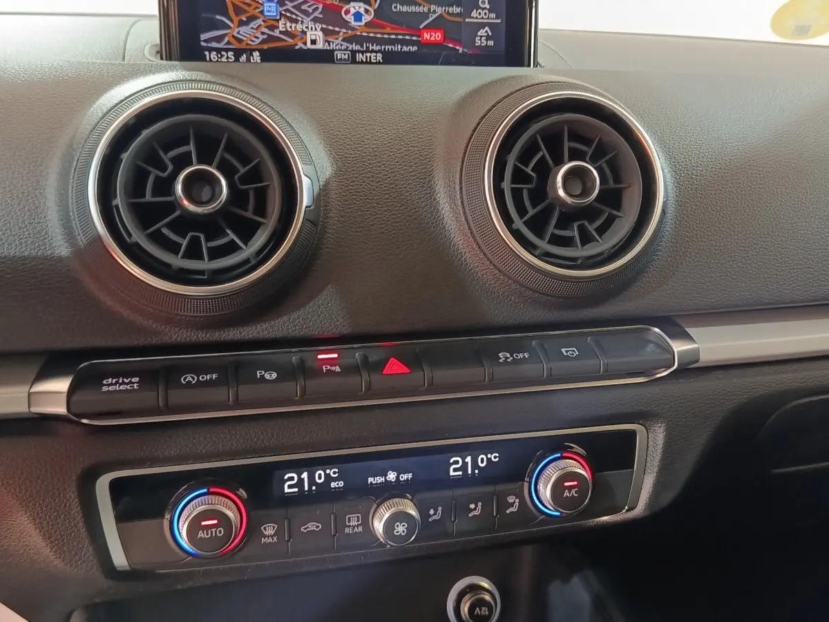 Vue rapprochée du tableau de bord de l’Audi A3 35 TDI 2020, montrant les aérateurs ronds et la climatisation digitale à 21°C.