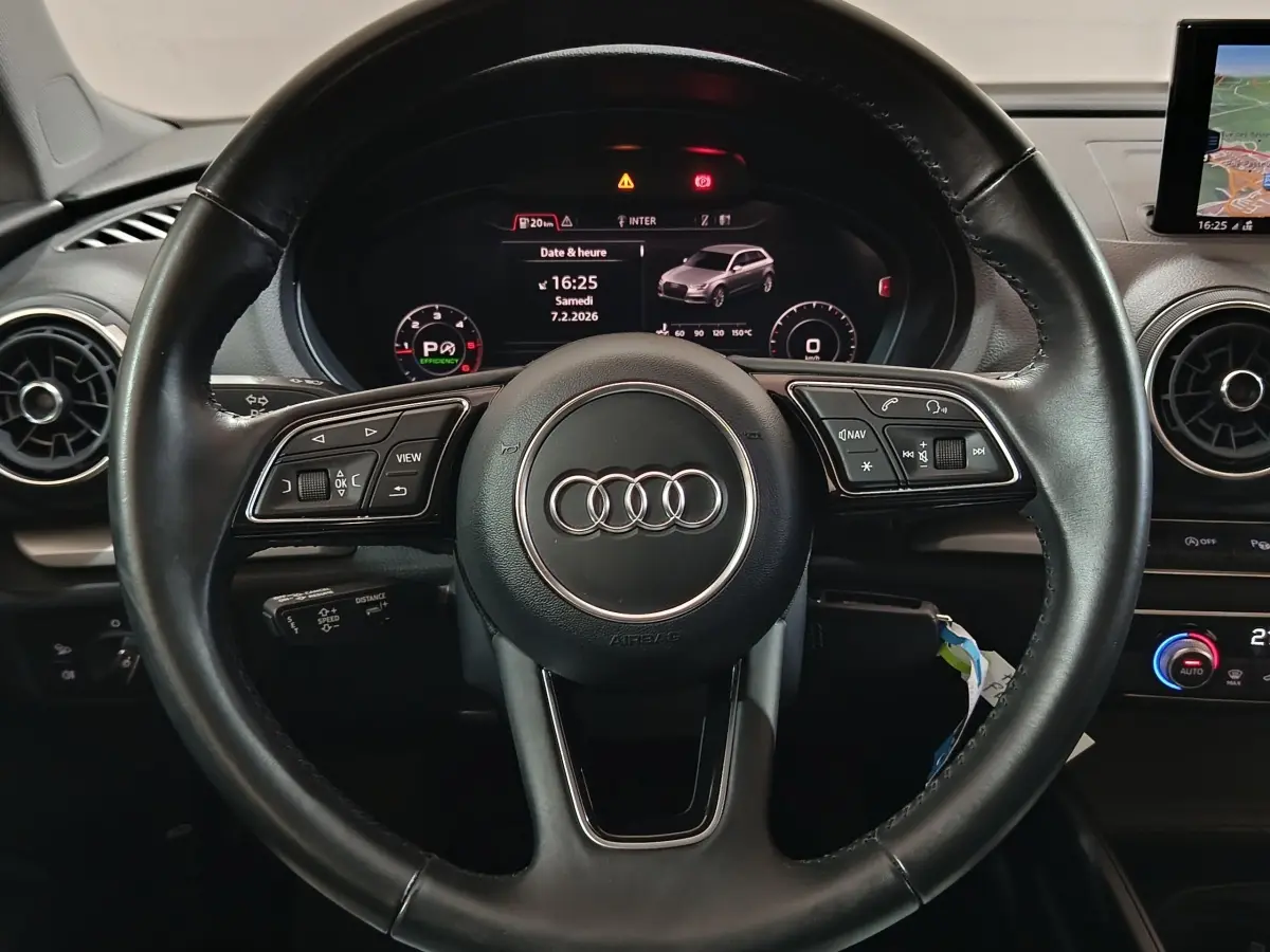 Vue intérieure centrée sur le volant cuir noir de l'Audi A3 35 TDI avec tableau de bord numérique et écran navigation.
