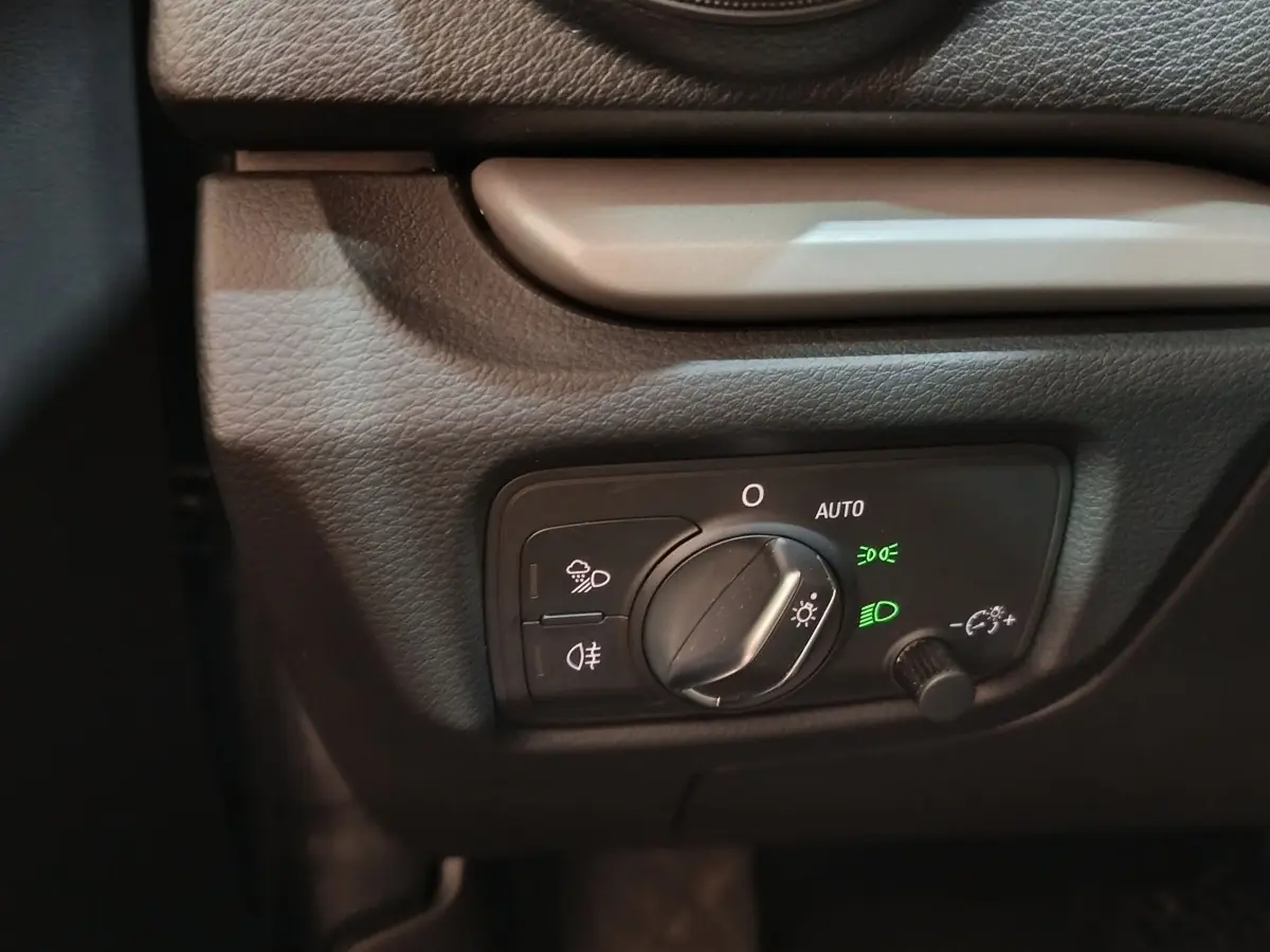 Gros plan sur le bouton de commande des phares avec réglage automatique dans l’habitacle gris foncé de l’Audi A3 35 TDI.