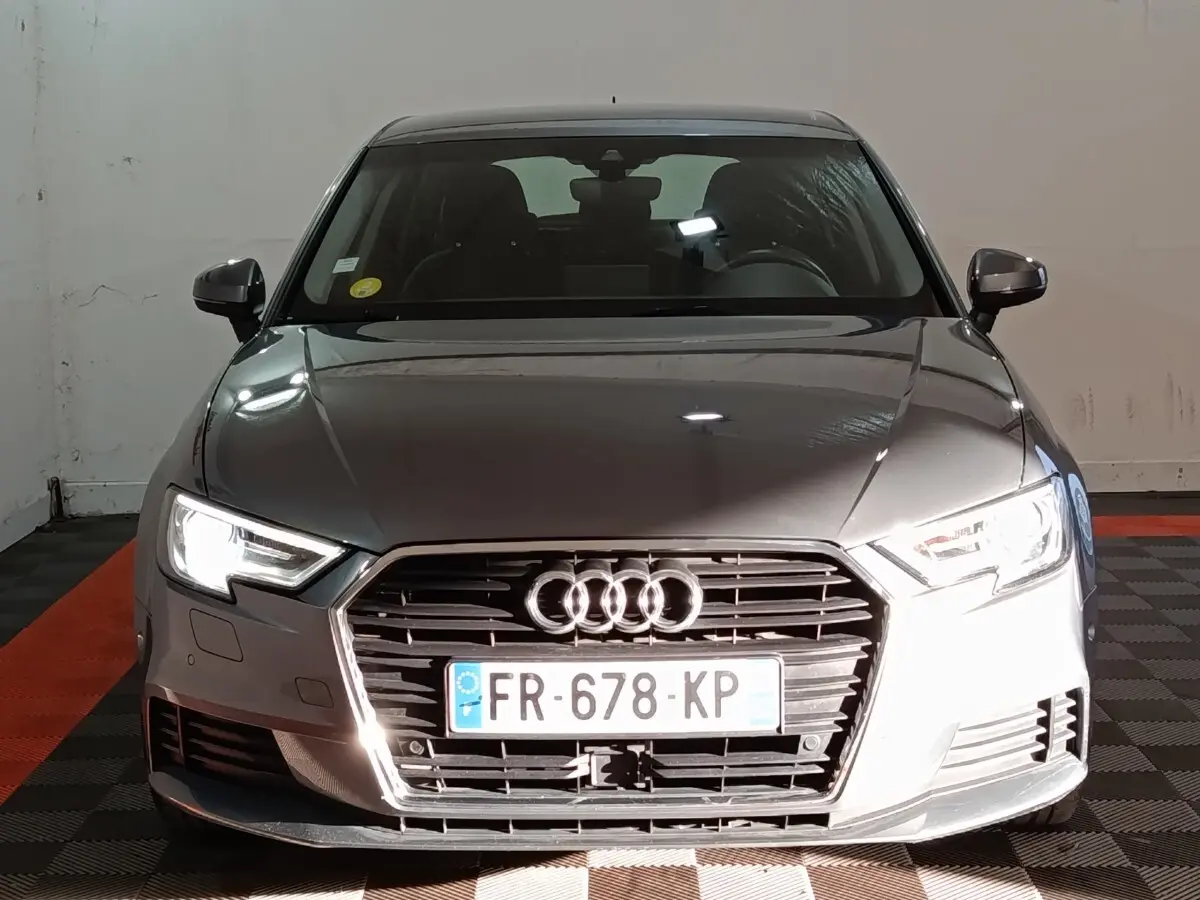 Vue de face d'une Audi A3 gris foncé avec phares allumés et calandre hexagonale distinctive.