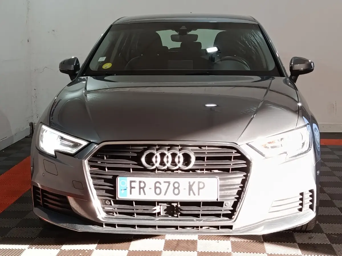 Vue frontale d'une Audi A3 gris foncé 35 TDI 150 S tronic avec phares LED allumés et calandre distinctive.
