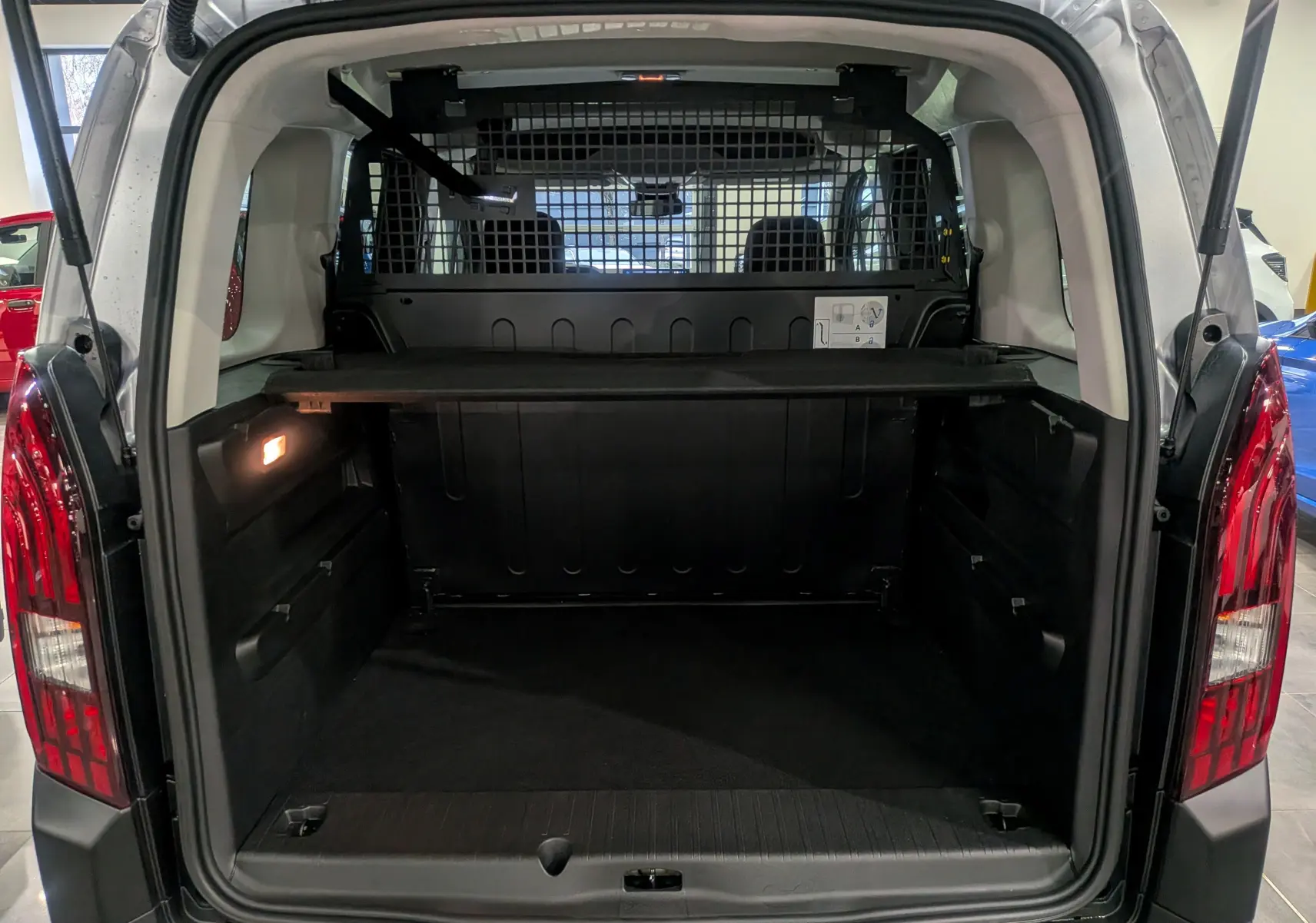 Vue arrière du coffre ouvert du Peugeot Rifter gris acier 2025, avec séparation grillagée et espace de chargement spacieux.