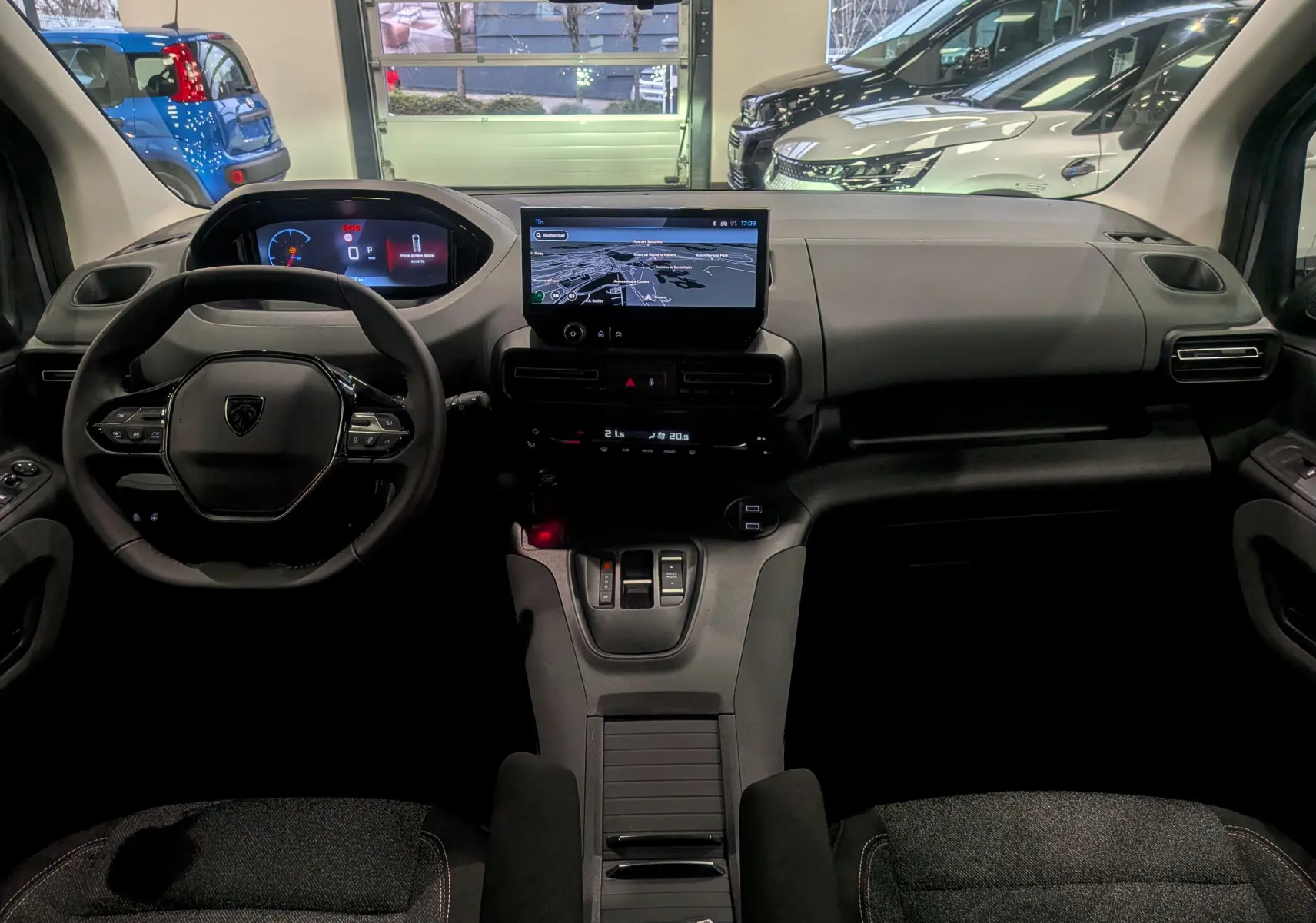 Vue intérieure frontale du Peugeot Rifter gris acier 2025, mettant en valeur le tableau de bord numérique et l'écran tactile central.