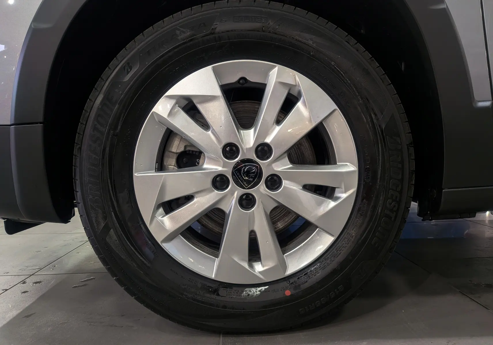 Gros plan sur la roue avant droite du Peugeot Rifter gris acier 2025 avec jante alliage et pneu Bridgestone.