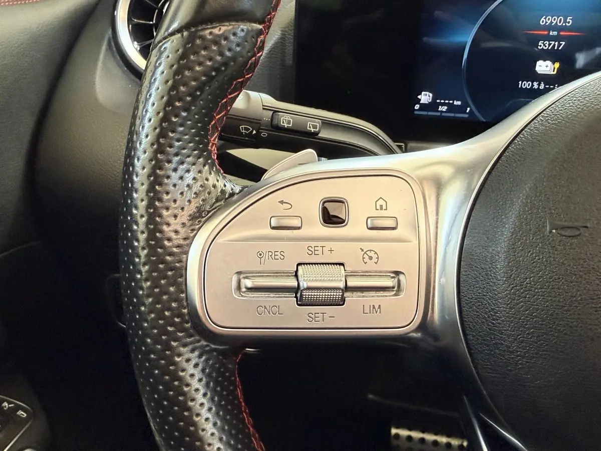 Gros plan sur le volant cuir perforé noir avec commandes argentées du Mercedes GLA 250 e AMG Line, affichage digital en arrière-plan.