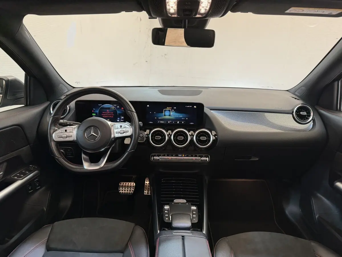 Vue intérieure avant du tableau de bord noir de la Mercedes GLA 250 e AMG Line avec volant cuir multifonctions et écran tactile.