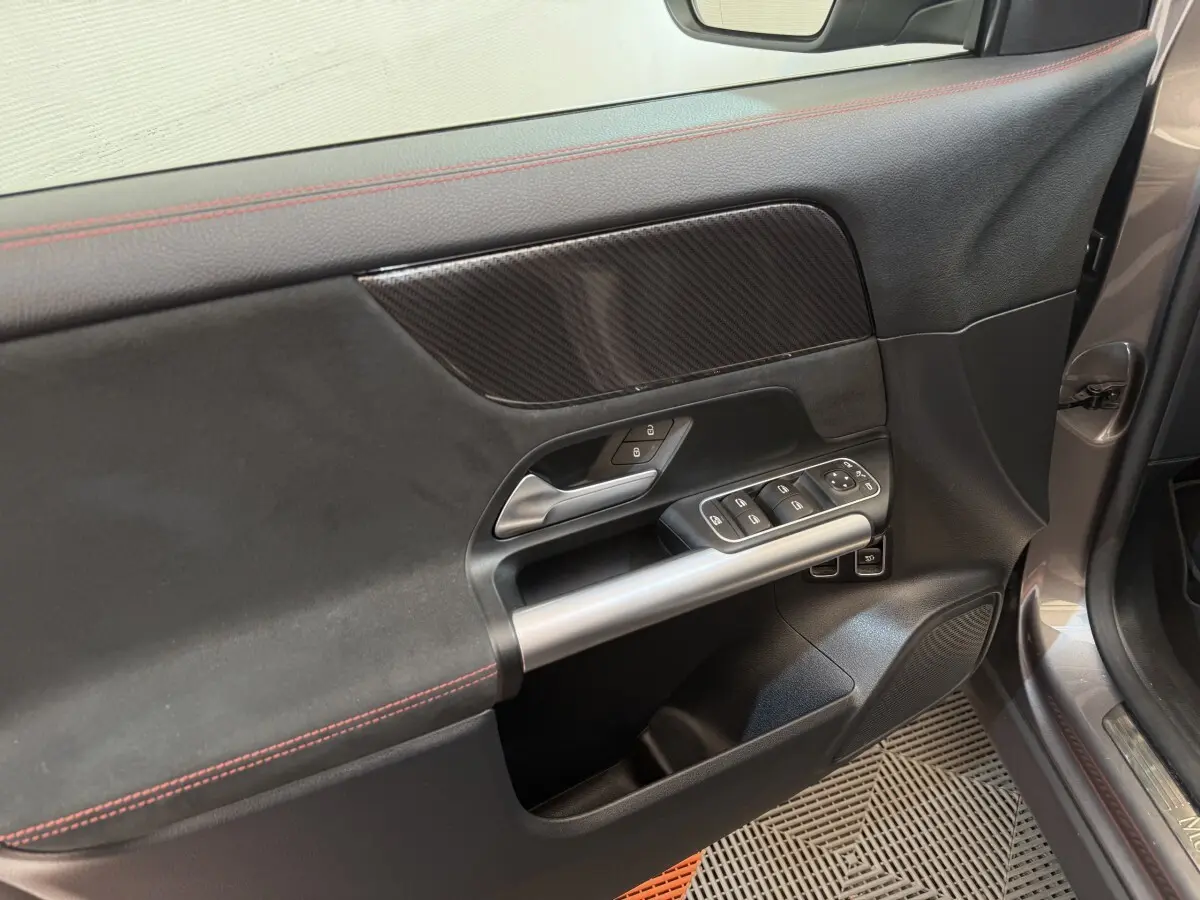 Vue rapprochée de la porte avant gauche gris clair du Mercedes GLA 250 e AMG Line avec garniture noire et surpiqûres rouges.