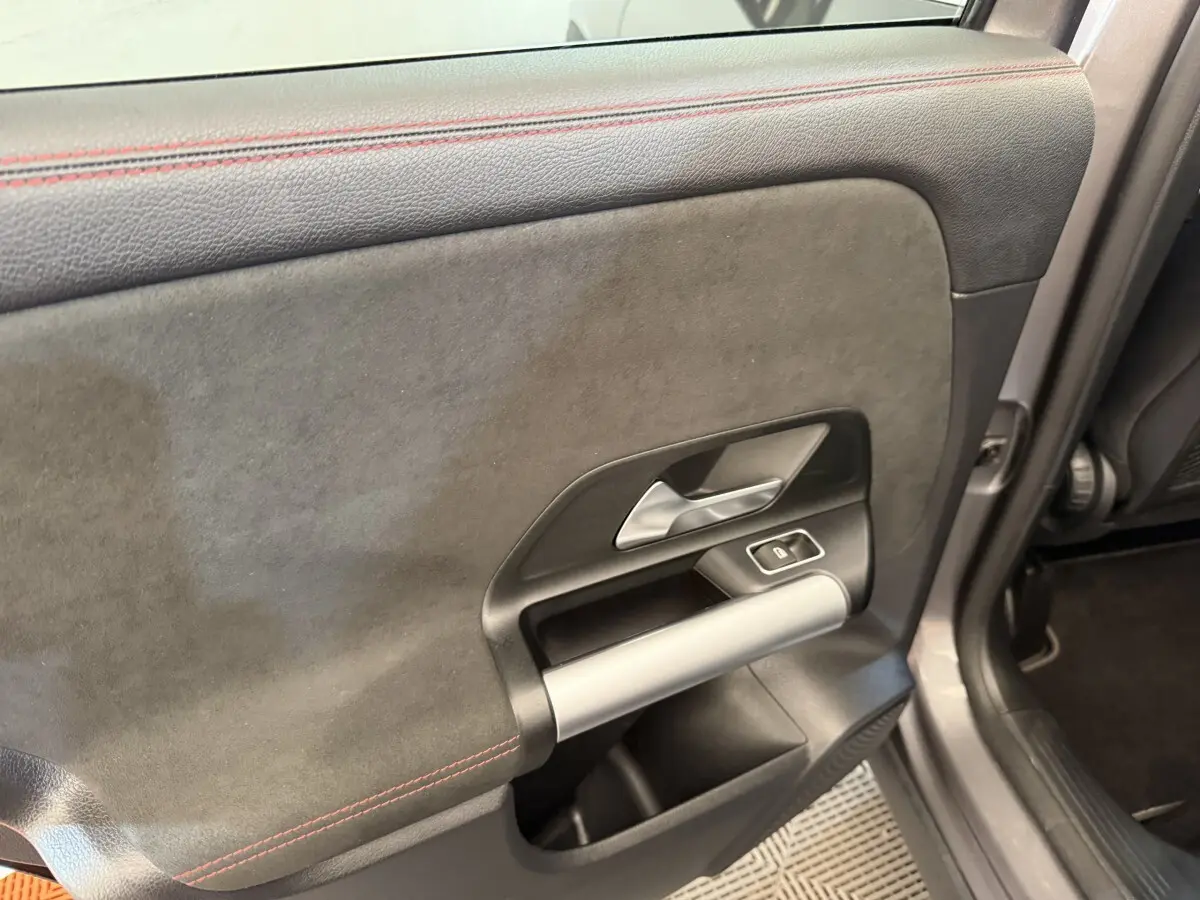 Gros plan sur la porte intérieure côté gauche du Mercedes GLA 250 e AMG Line gris clair, avec surpiqûres rouges et poignée argentée.
