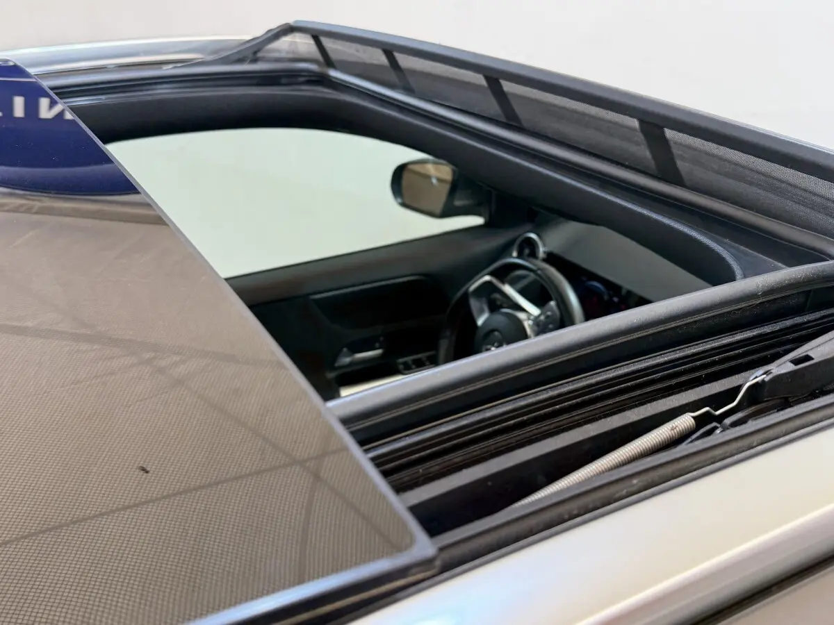 Vue rapprochée du toit ouvrant ouvert et intérieur côté conducteur d’une Mercedes GLA 250 e AMG Line gris clair.