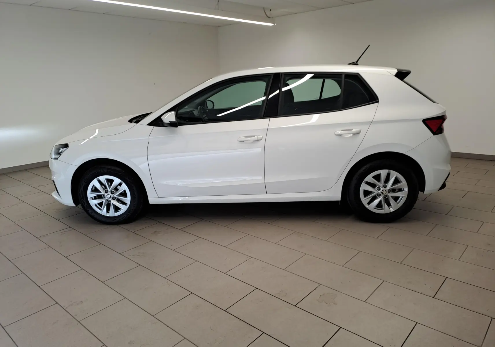 Vue latérale droite d'une Skoda Fabia blanche Candy 2023, finition Ambition, en intérieur sur sol carrelé.