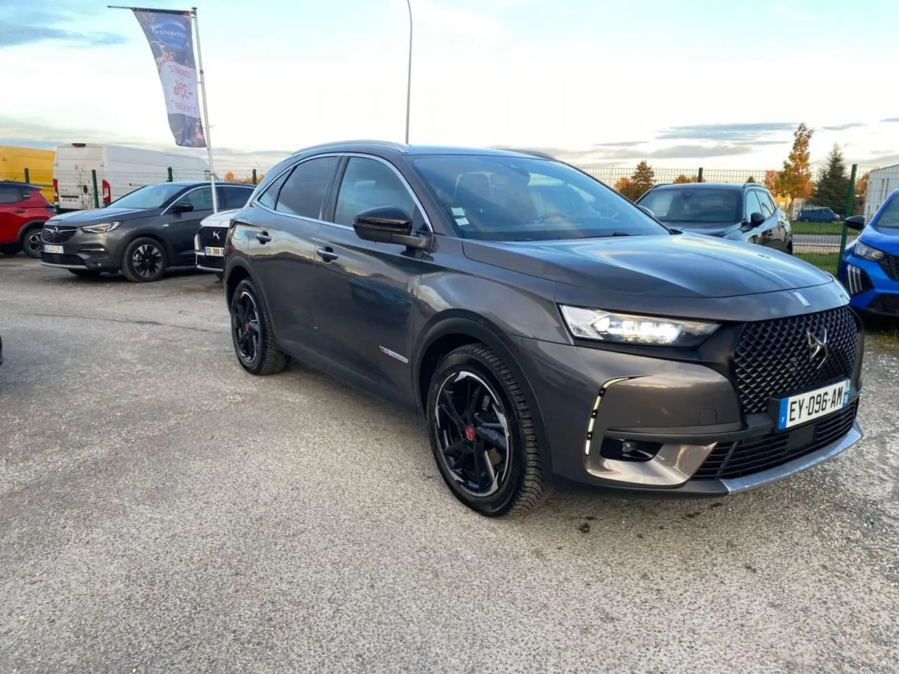 DS7 Crossback gris foncé en 3/4 avant droit, avec calandre noire et jantes noires brillantes sur parking extérieur.