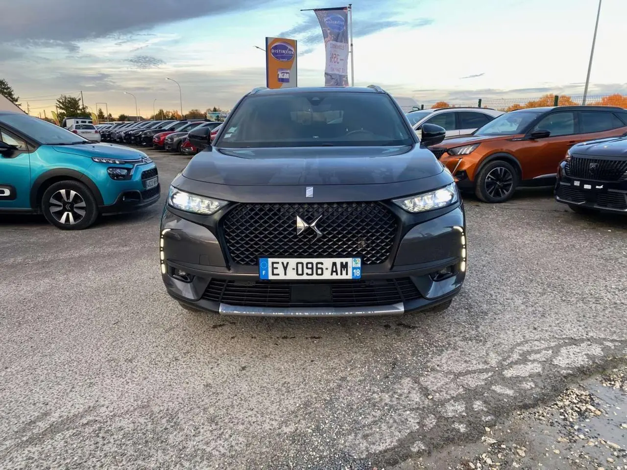 Vue frontale d'un DS7 Crossback gris foncé 2018 avec calandre noire et feux LED allumés sur un parking.