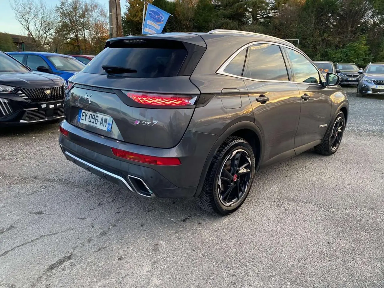 DS7 Crossback gris foncé en 3/4 arrière droit, avec feux arrière allumés et jantes noires distinctives.