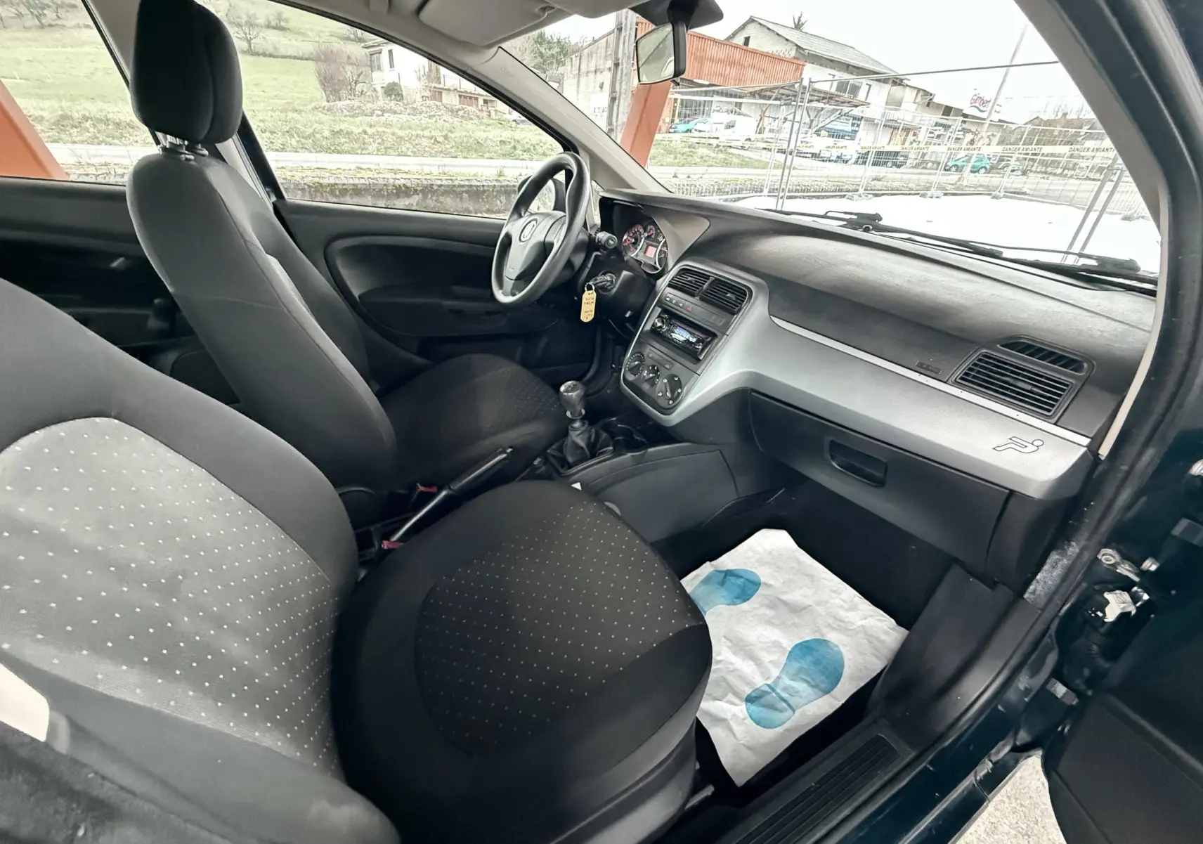 Vue intérieure côté conducteur de la Fiat Punto noire 2009, montrant le tableau de bord et les sièges en tissu noir.