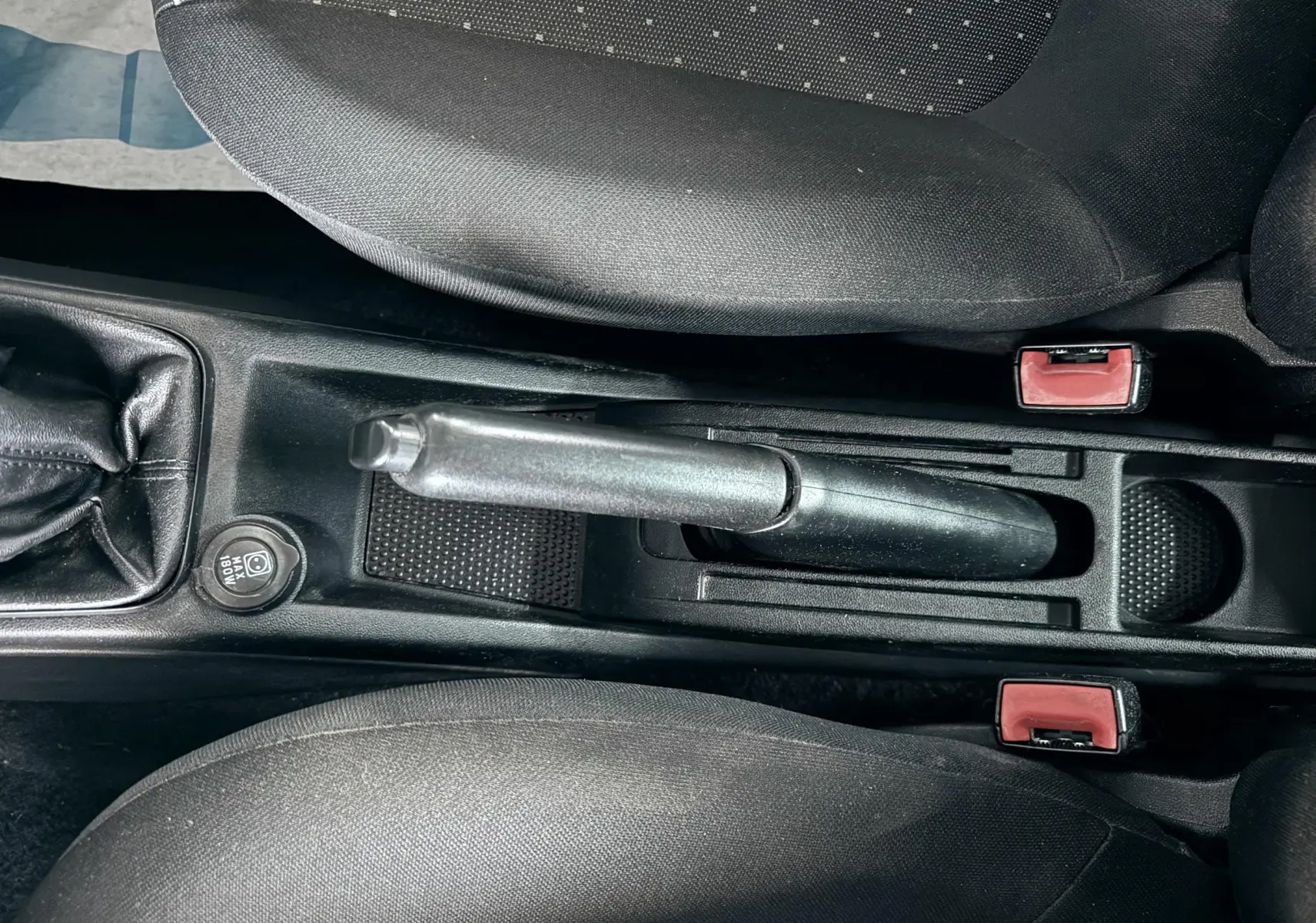 Vue plongeante sur le frein à main et la console centrale noire de la Fiat Punto 1.2 i 65 de 2009, avec sièges tissu gris.