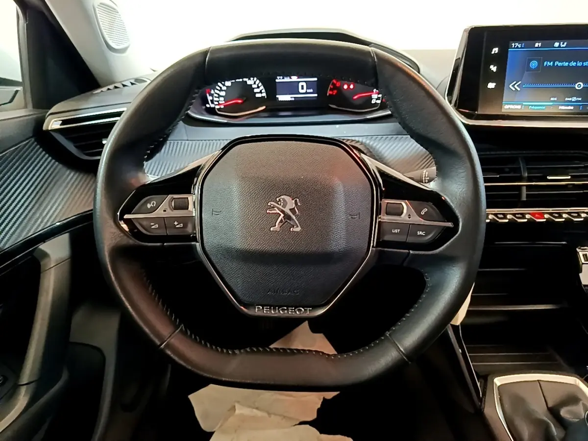 Vue intérieure centrée sur le volant cuir noir de la Peugeot 2008 avec tableau de bord digital et écran tactile.
