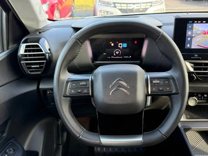 Vue frontale du volant noir du Citroën C4 2024 gris, avec commandes intégrées et tableau de bord numérique.