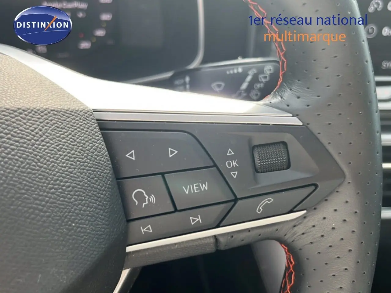 Gros plan sur le volant perforé avec surpiqûres rouges du SEAT LEON ST gris magnétique, montrant les commandes multifonctions.