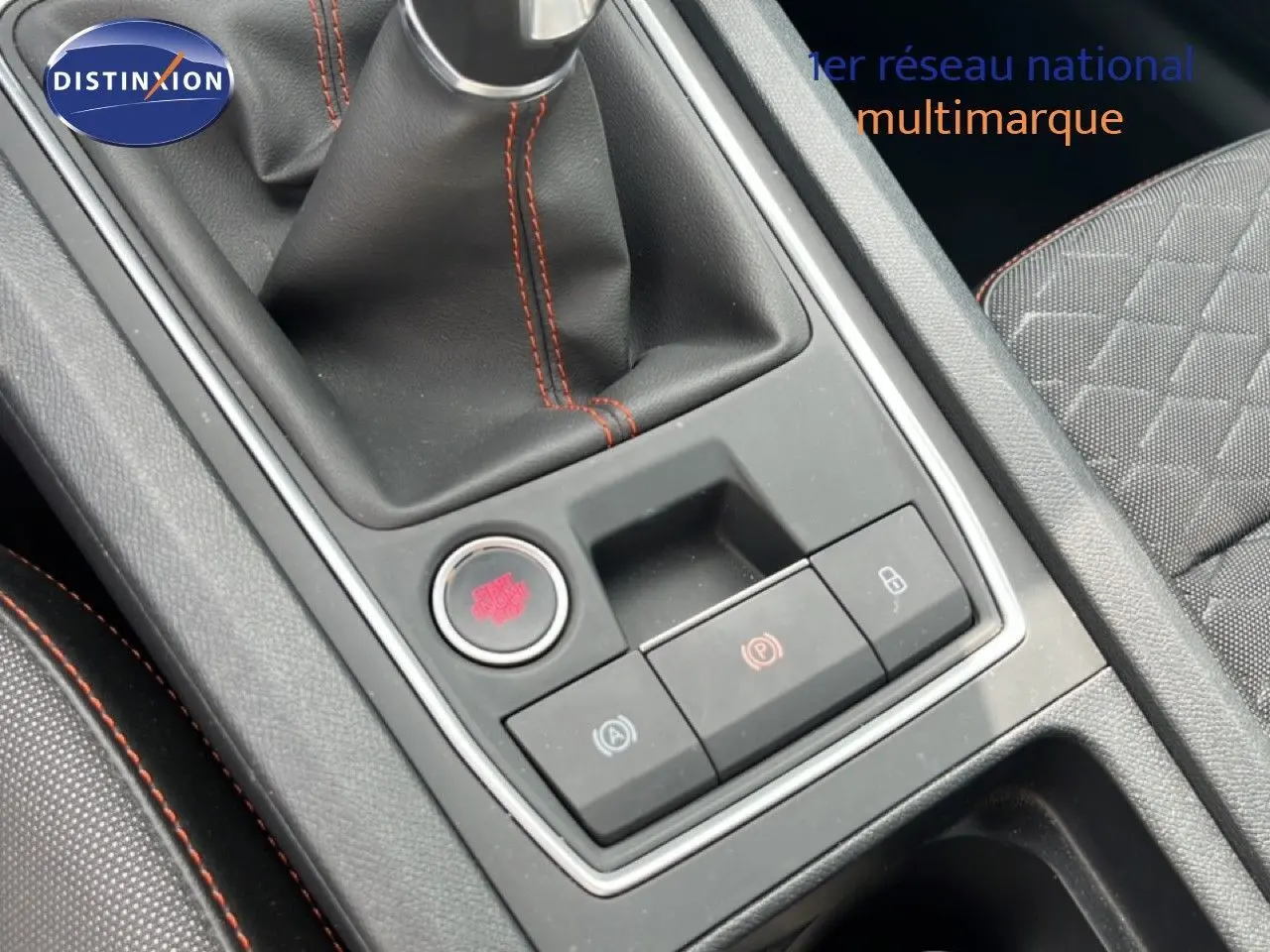 Gros plan sur la console centrale avec levier de vitesse et boutons de contrôle, intérieur tissu gris avec surpiqûres rouges.
