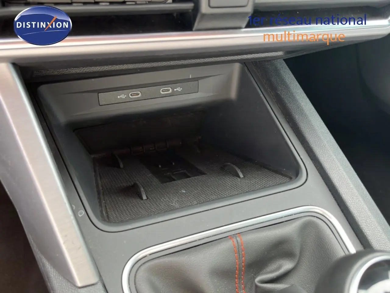 Gros plan sur la console centrale d’une SEAT Leon ST 2025, montrant les ports USB et le soufflet de levier de vitesses noir avec surpiqûres rouges.