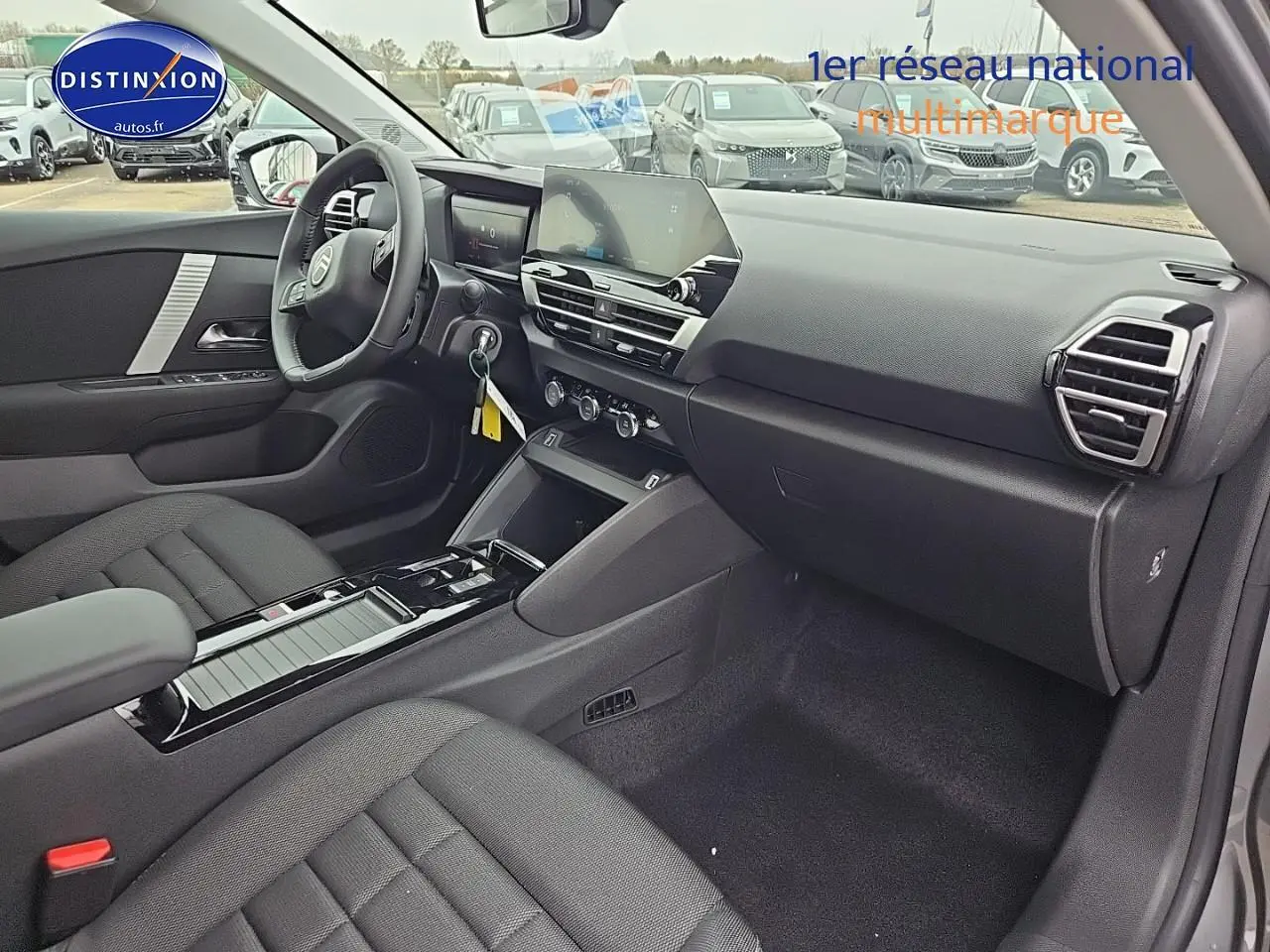 Intérieur avant droit de la Citroën C4 1.2 hybride 136 plus 2025, avec tableau de bord moderne et sièges tissu noir.