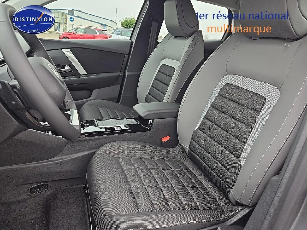 Intérieur de la Citroën C4 hybride 2025, vue côté conducteur sur sièges tissu noir et gris avec accoudoir central.