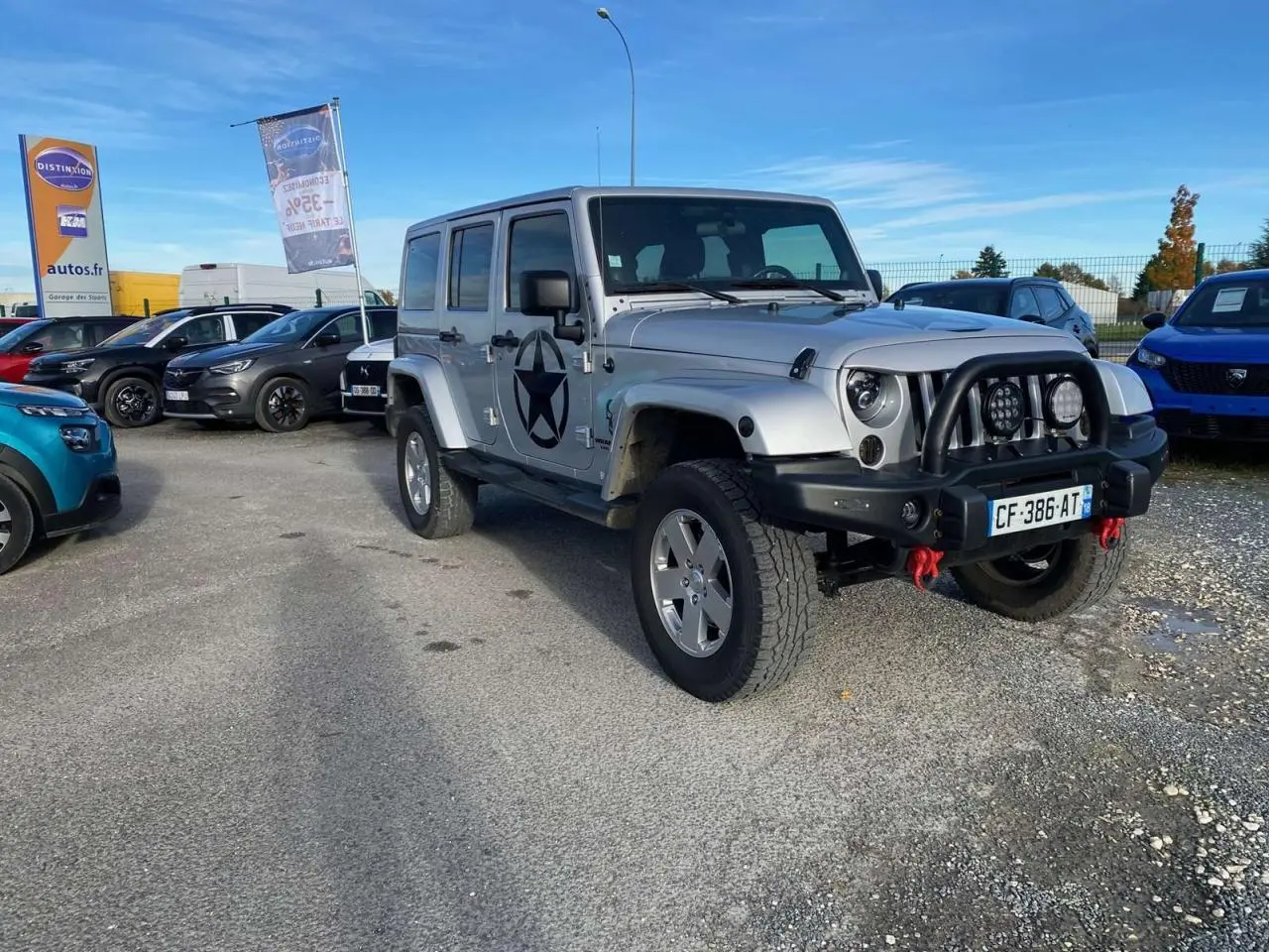 Jeep Wrangler gris clair vue 3/4 avant droit avec étoile noire sur porte et pare-buffle équipé de phares additionnels.