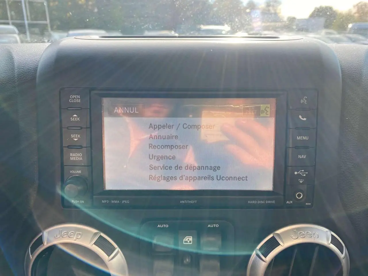 Écran central tactile du système Uconnect sur Jeep Wrangler gris clair 2012, avec commandes autour et reflets lumineux.