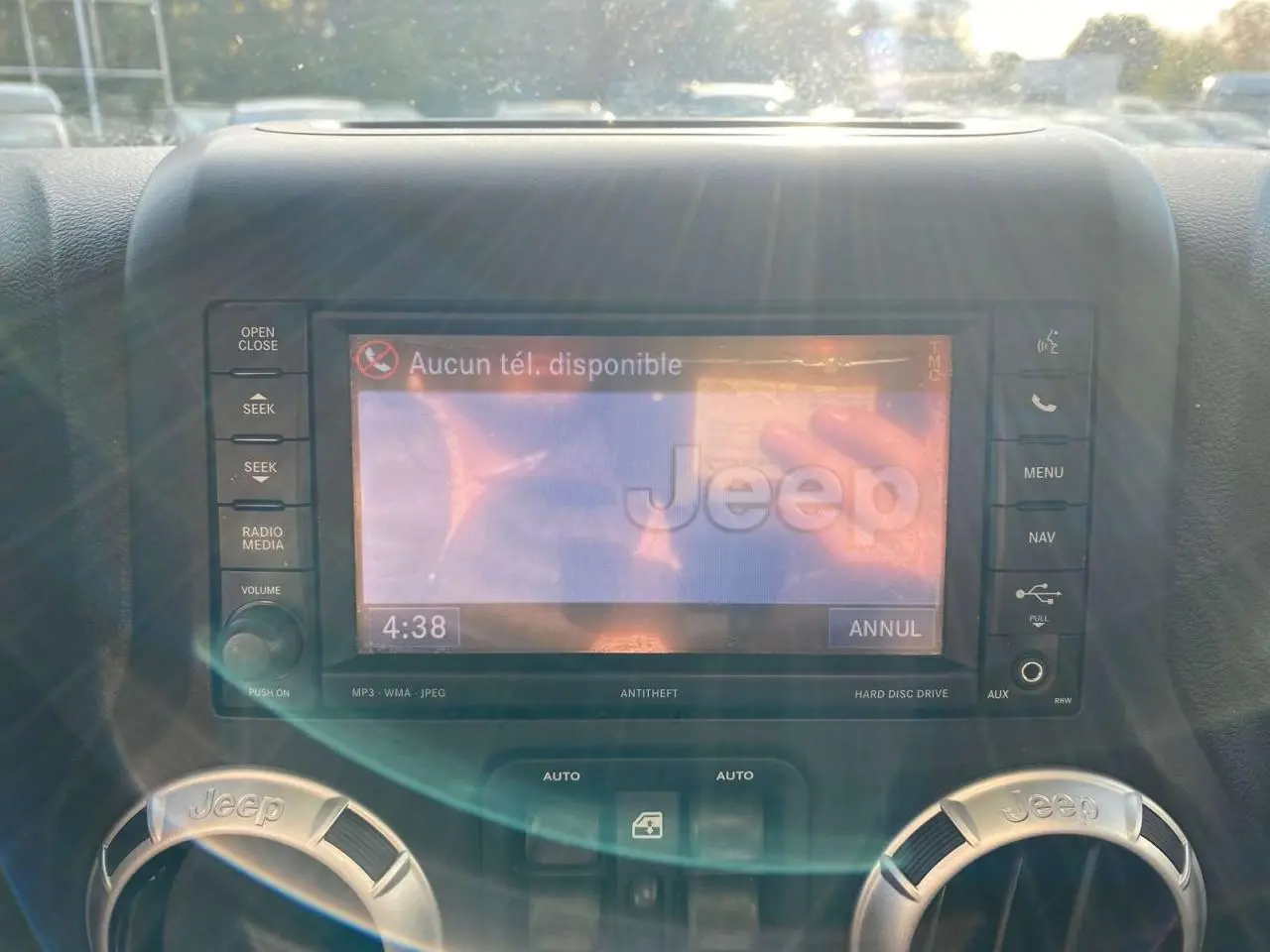 Détail de l'écran multimédia et des aérateurs marqués Jeep dans l'habitacle d'un Wrangler gris clair 2012.