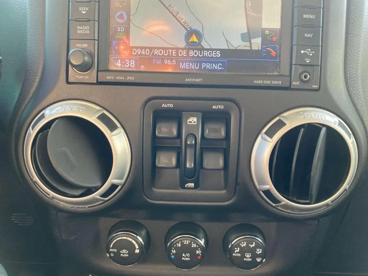 Vue rapprochée du tableau de bord du Jeep Wrangler gris clair 2012, montrant les aérateurs ronds et la console centrale avec commandes.