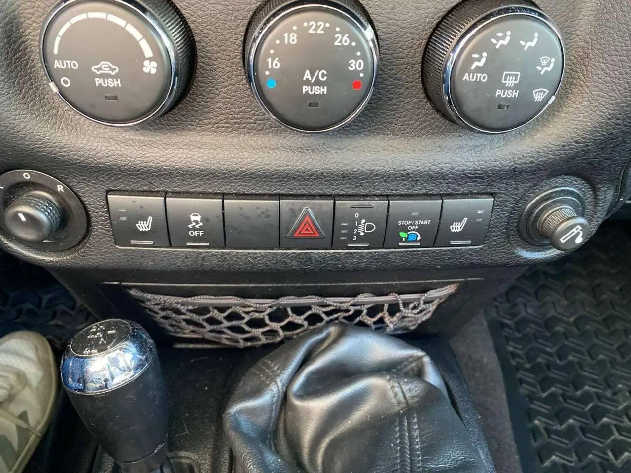 Gros plan sur la console centrale du Jeep Wrangler 2012 gris clair, montrant la boîte manuelle et les commandes de climatisation.