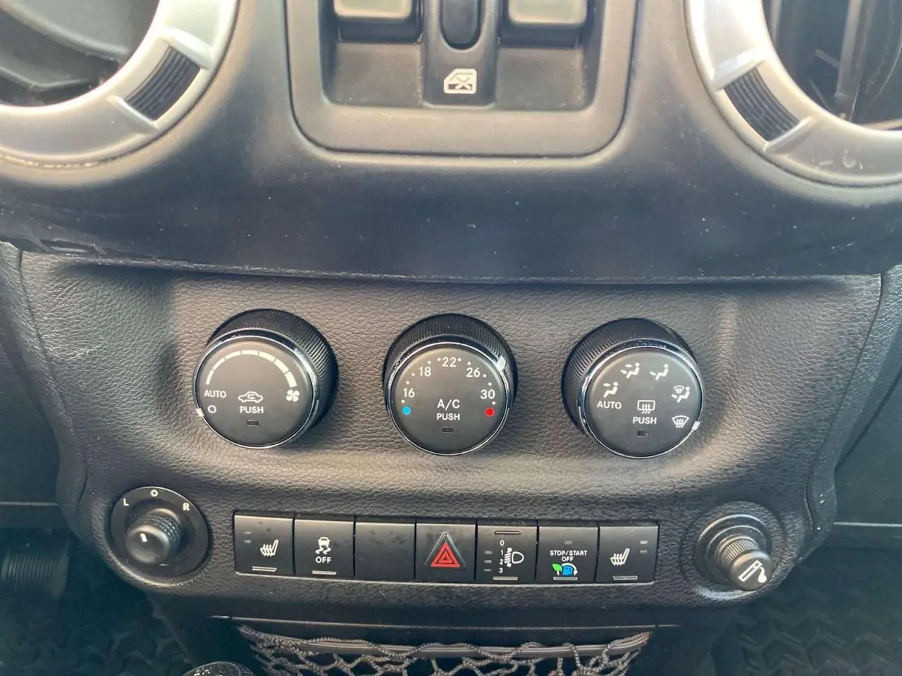 Gros plan sur les commandes de climatisation et les boutons de fonction du tableau de bord du Jeep Wrangler gris clair 2012.