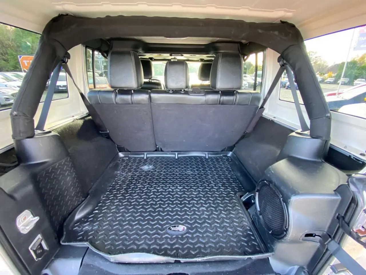 Vue intérieure arrière du coffre d'un Jeep Wrangler gris clair 2012 avec banquette et tapis de sol caoutchouc.