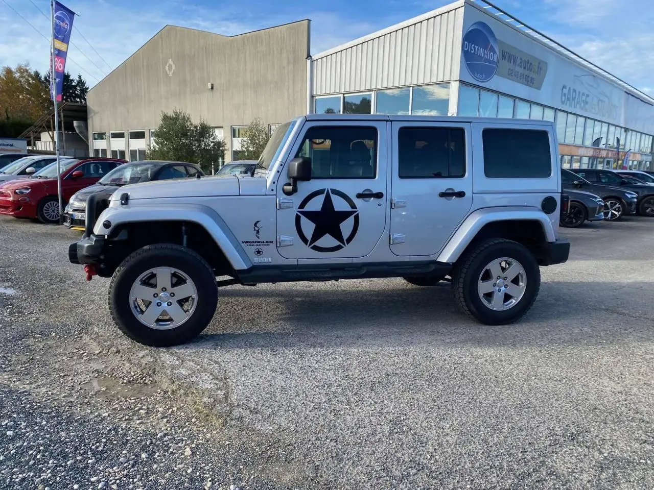 Profil côté gauche d'un Jeep Wrangler gris clair 2012 avec étoile noire militaire sur la porte, stationné en extérieur.