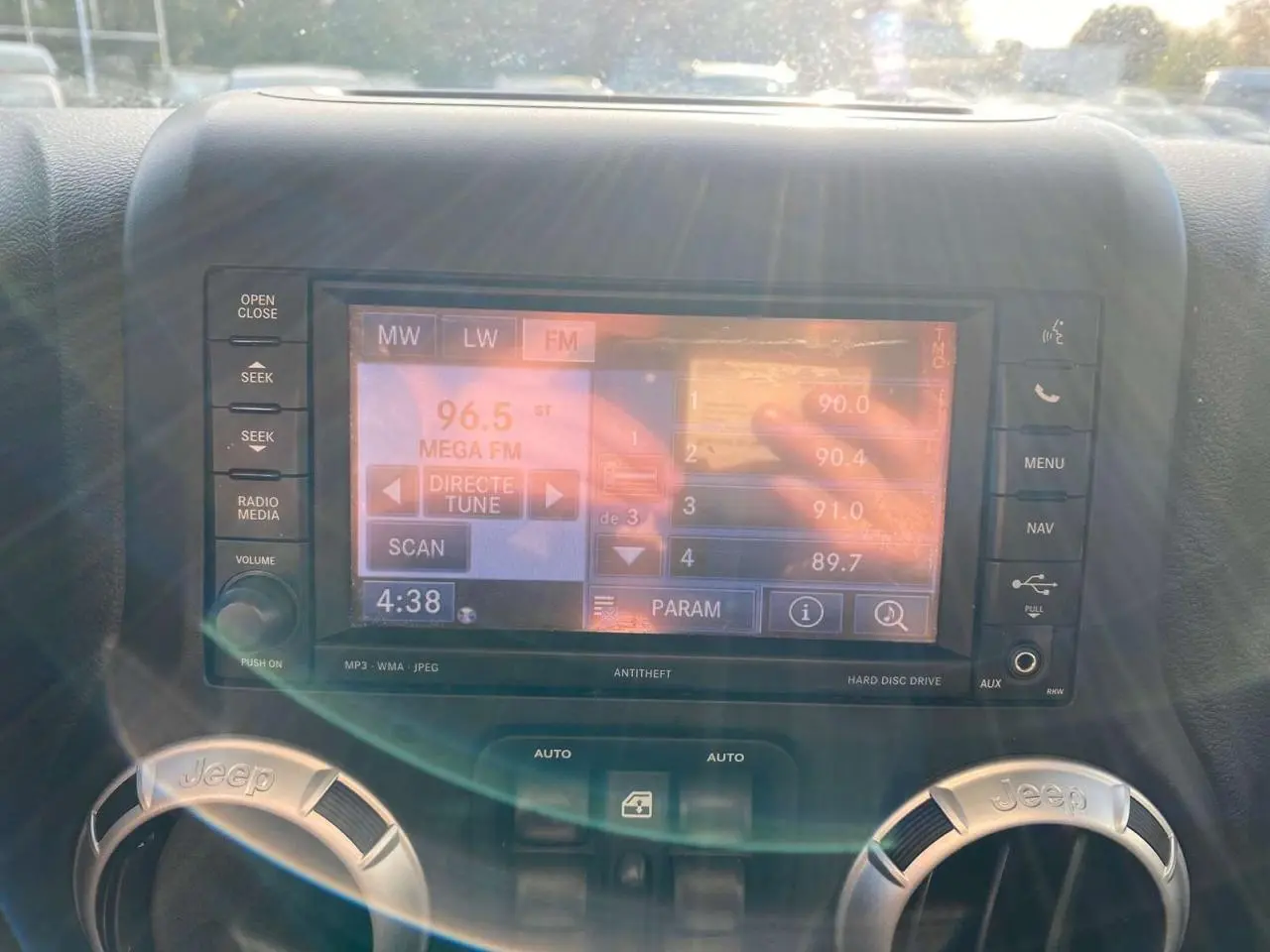 Écran multimédia allumé au centre du tableau de bord d'un Jeep Wrangler gris clair de 2012, avec commandes autour.