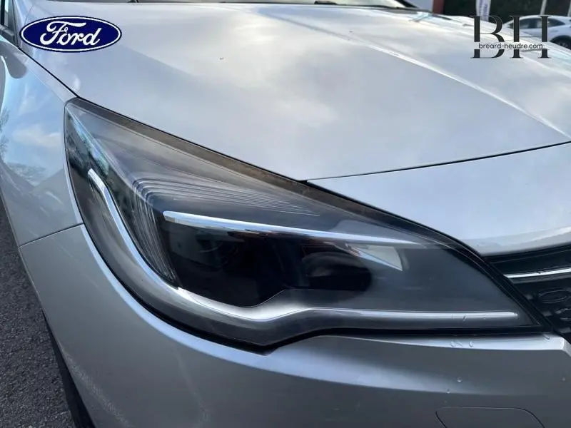 Gros plan sur le phare avant gauche d'une Opel Astra gris minéral, mettant en valeur les lignes modernes du bloc optique.