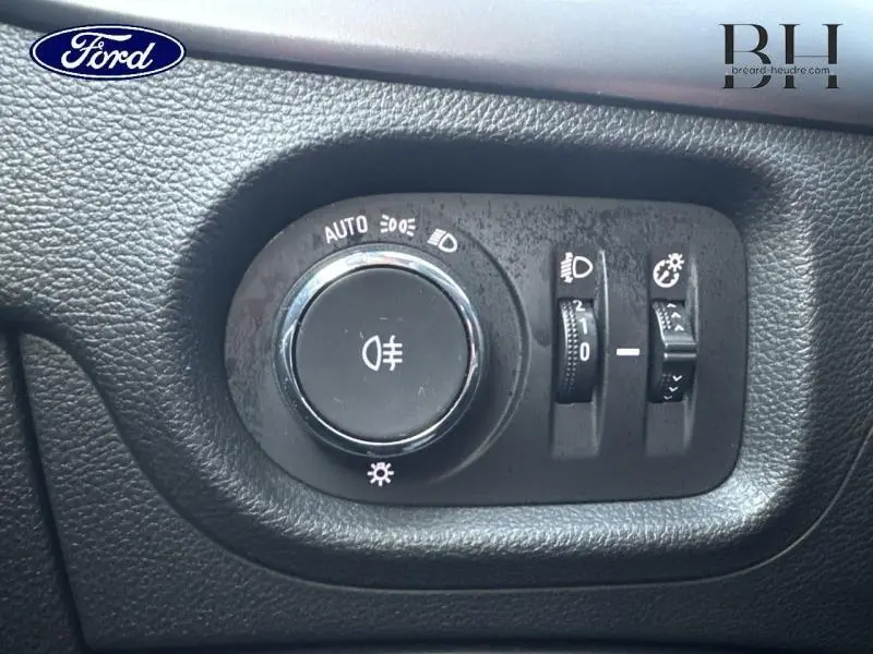 Gros plan sur le bouton de commande des phares et réglages lumineux d'une Opel Astra gris minéral, intérieur noir texturé.