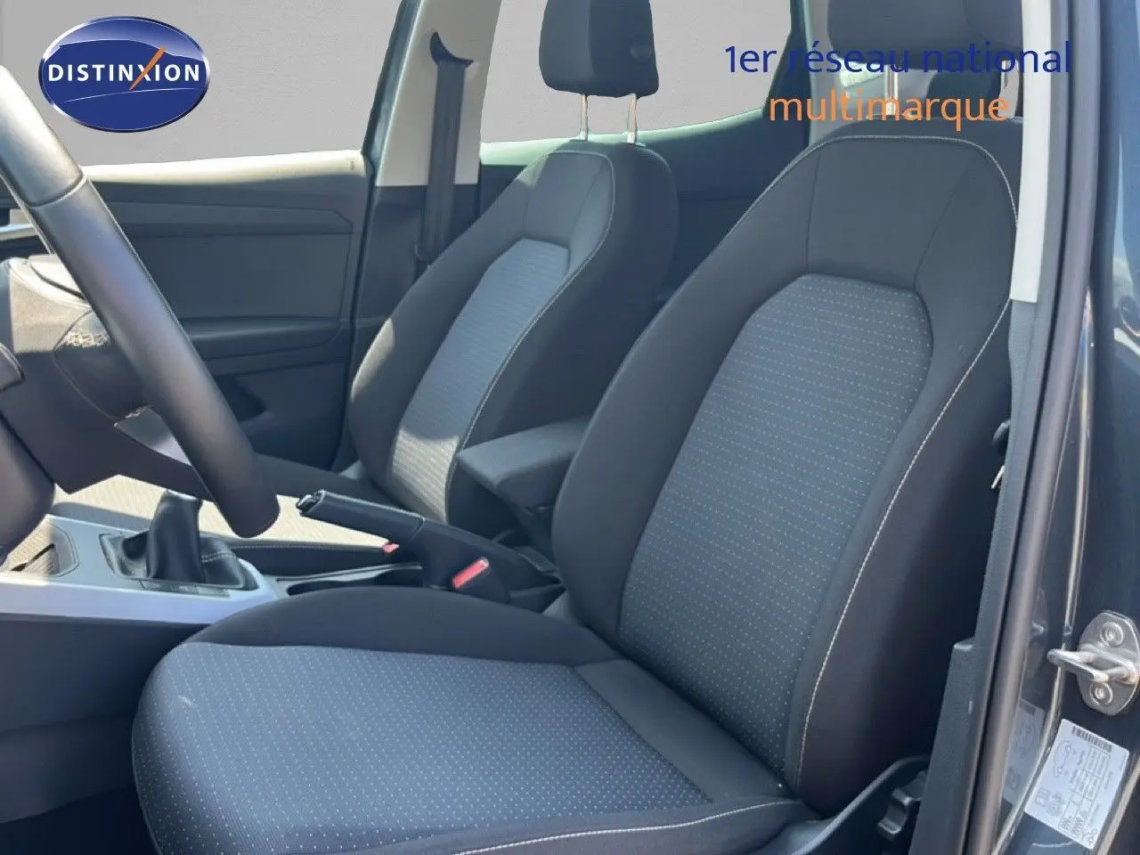 Vue intérieure côté conducteur du SEAT Arona gris magnetic, montrant les sièges tissu gris et noir avec coutures contrastées.