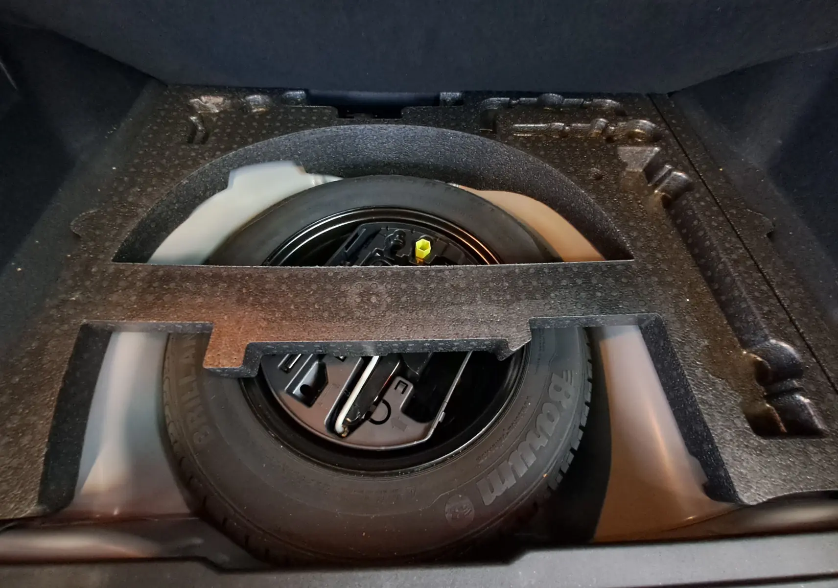 Vue plongeante sur la roue de secours noire et ses outils dans le coffre d'un Peugeot 2008 gris 2019.