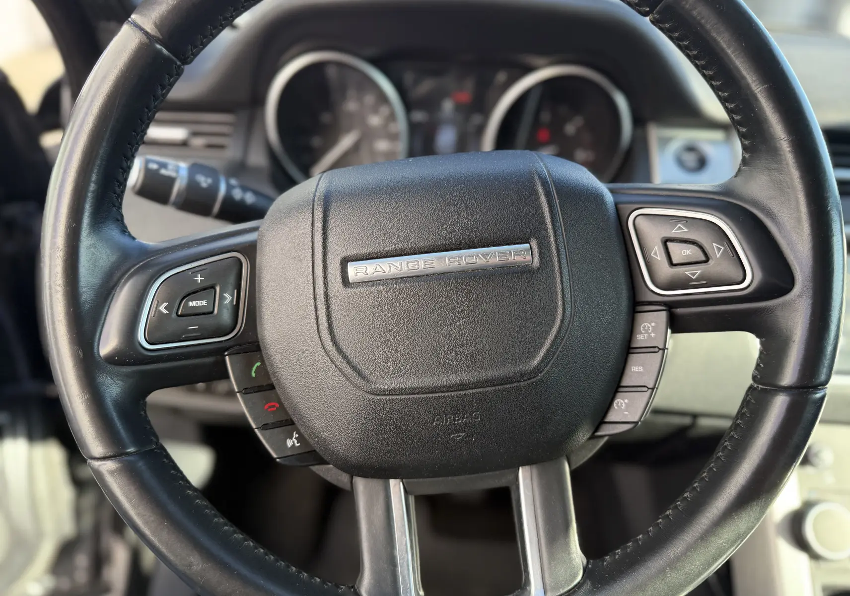 Gros plan sur le volant noir du Range Rover Evoque gris, avec commandes intégrées et logo central argenté.