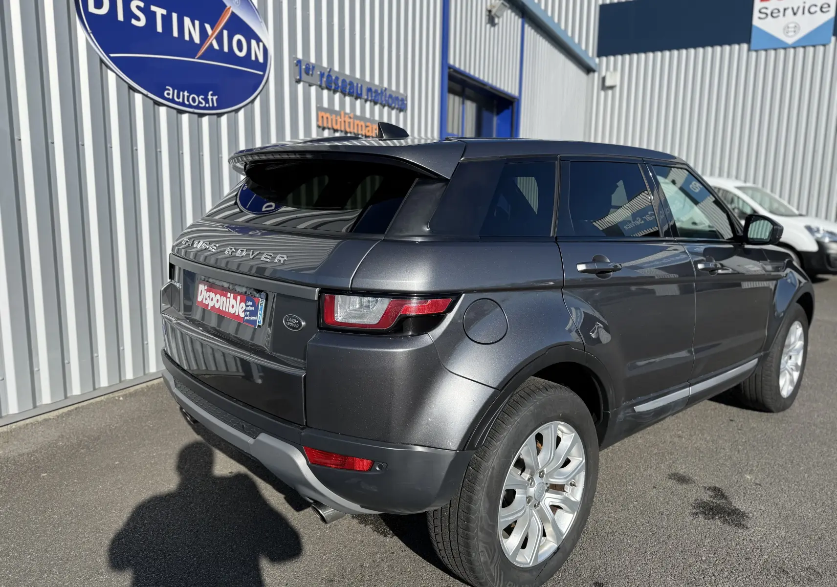 Vue 3/4 arrière droite d'un Range Rover Evoque gris métallisé garé devant un bâtiment commercial.