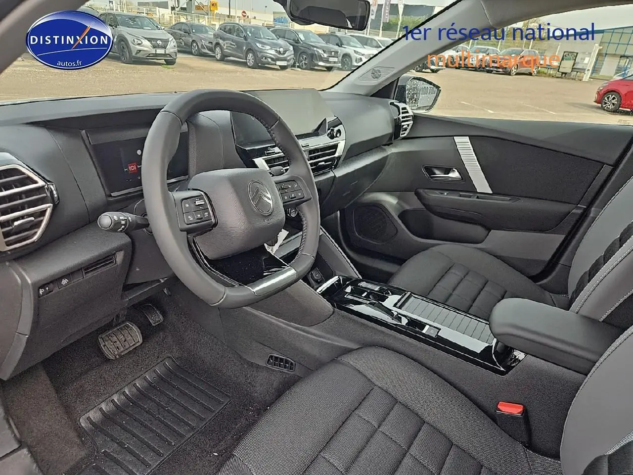 Intérieur avant droit de la Citroën C4 blanc okenite 2025, volant cuir, console centrale brillante et sièges tissu noir