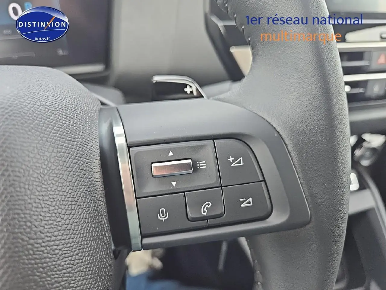 Gros plan sur les commandes audio et vocales au volant cuir de la Citroën C4 blanche Okenite 2025.