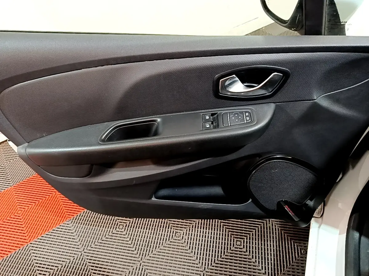 Vue intérieure du panneau de porte avant gauche d'une Renault Clio blanche, avec commandes électriques et haut-parleur intégré.