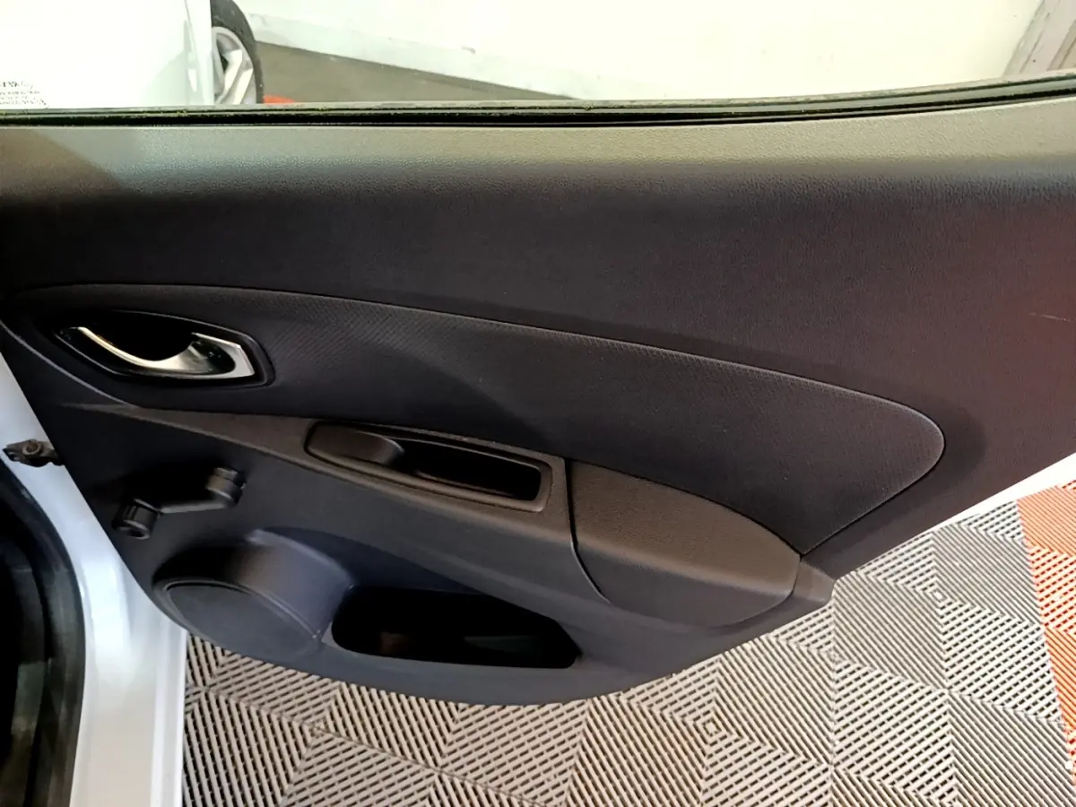 Vue intérieure de la porte côté gauche d'une Renault Clio Zen Energy dCi 75 blanche, avec poignée chrome et manivelle de vitre.