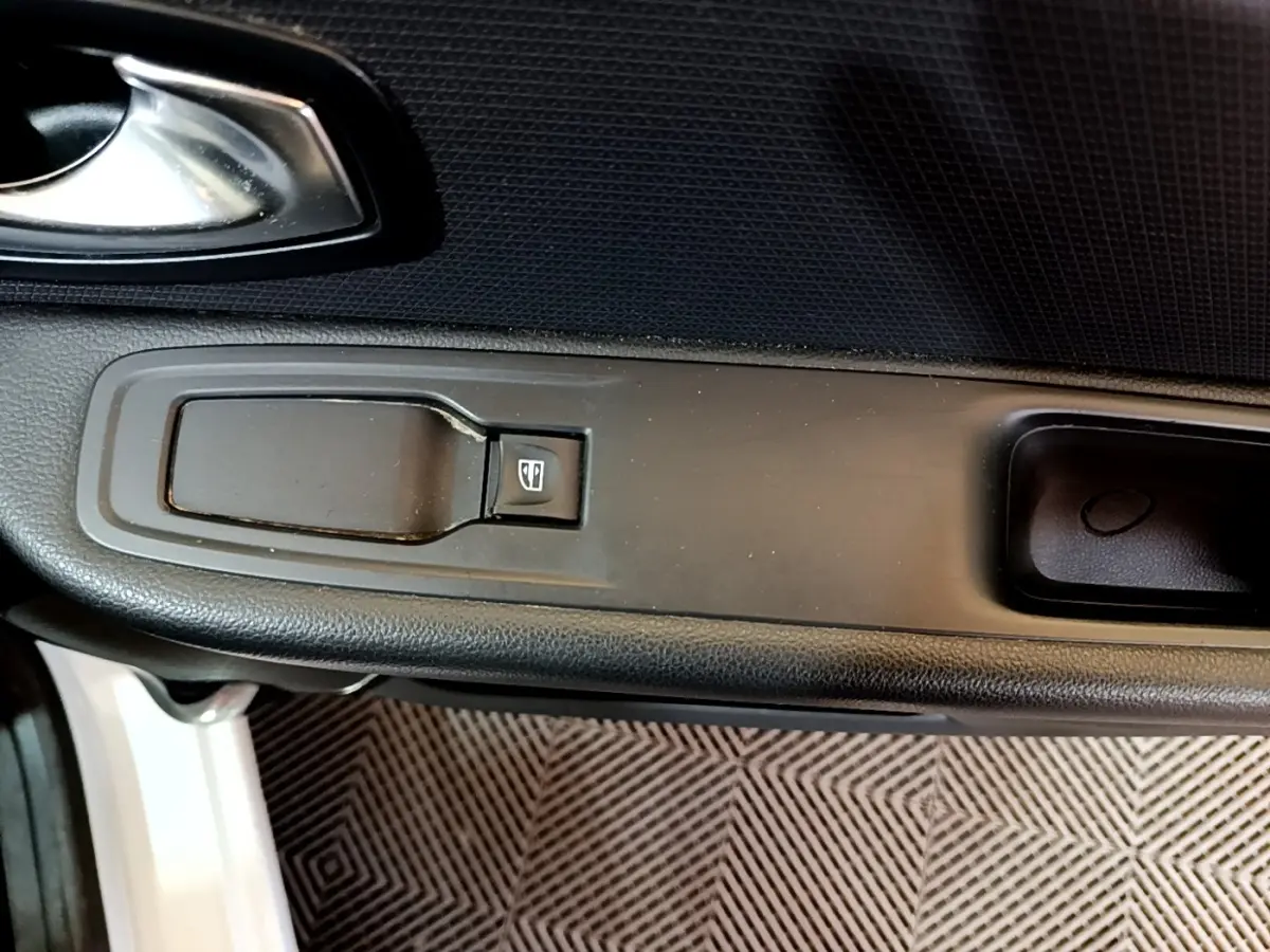 Gros plan sur la commande de lève-vitre côté conducteur de la Renault Clio blanche, avec poignée de porte noire.