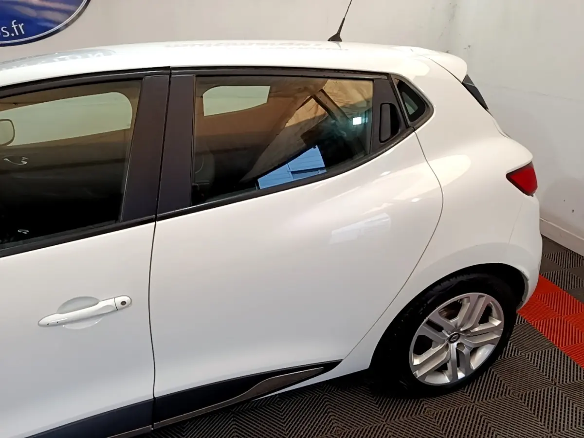 Profil arrière droit d'une Renault Clio Zen Energy dCi 75 blanche, avec poignées de porte intégrées et jantes alliage visibles.