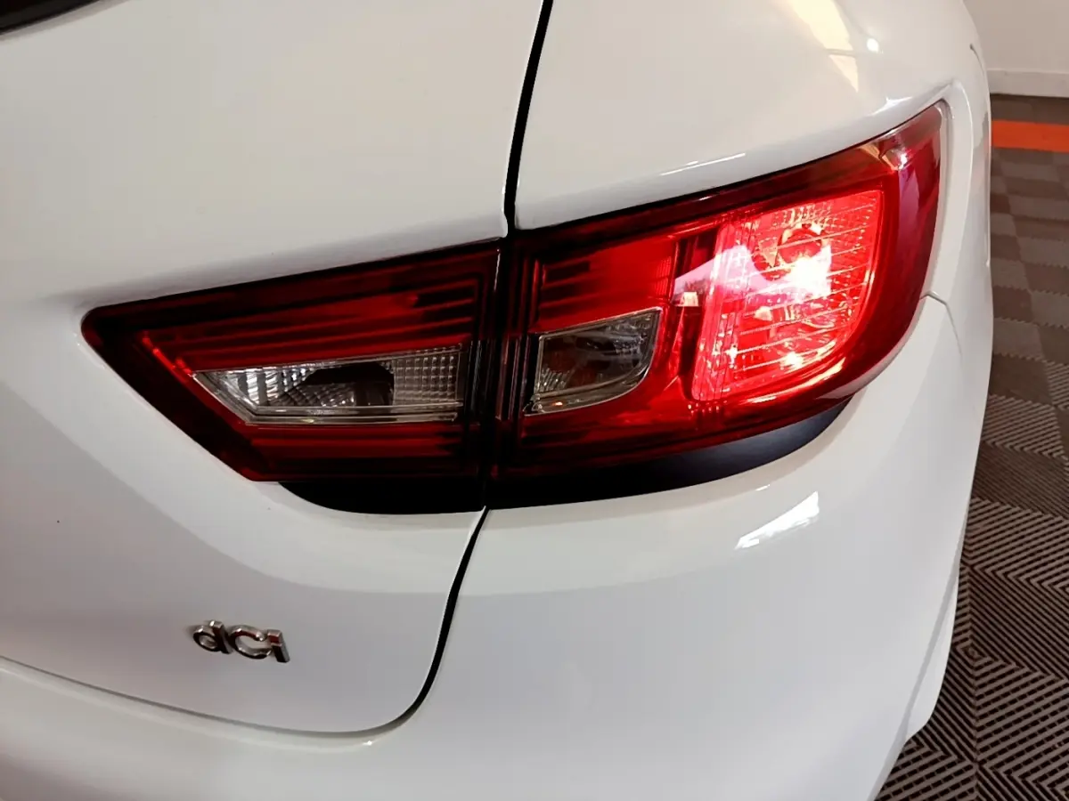 Gros plan sur le feu arrière droit rouge et blanc d'une Renault Clio blanche avec logo dCi visible sur le coffre.