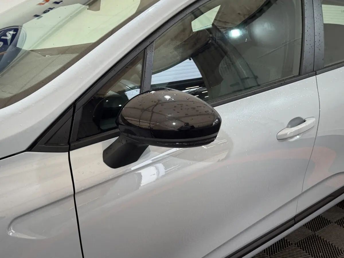 Rétroviseur noir brillant côté gauche d'une Renault Clio gris clair vue de profil avant en intérieur.