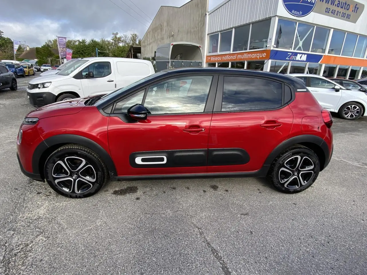 Profil latéral gauche d'une Citroën C3 rouge Elixir avec toit noir et protections latérales noires distinctives.